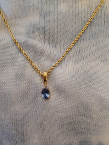 Reviewer's gold Oval Birthstone Charm with a blue stone worn on a rope chain against a light sweater.