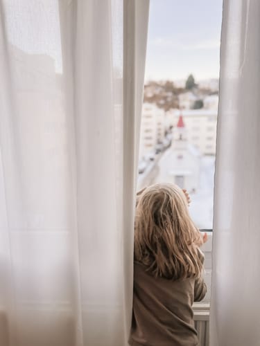 Reviewer's photo of a child looking out a window, enhanced with the warm, golden Family Fun Lightroom Presets.