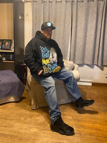 Reviewer sitting indoors wearing the black DopeSkill Hoodie, paired with blue jeans and matching black sneakers.