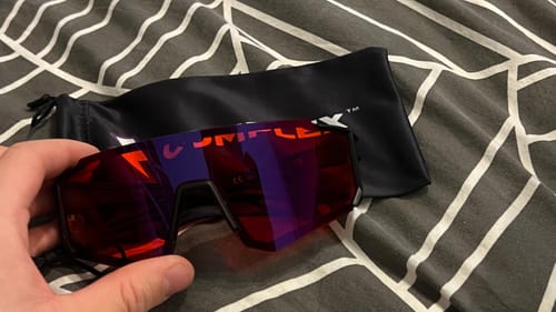 Customer holding the red-lensed HyperX glasses, with the black carrying pouch shown in the background.
