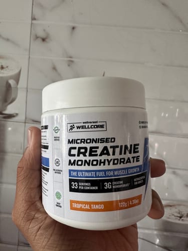 Reviewer holding a white tub of Wellcore Micronised Creatine Monohydrate in the Tropical Tango flavor.