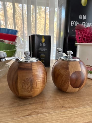 Ein Kunde zeigt die zwei runden Salz- und Pfeffermühlen aus Holz auf einem Küchentisch.
