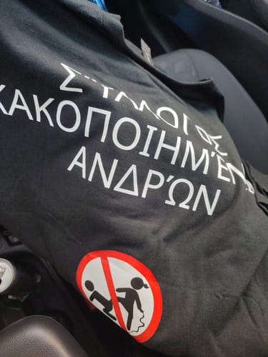 Customer's black unisex T-shirt with white Greek text and a graphic showing one figure kicking another inside a 'no' symbol.