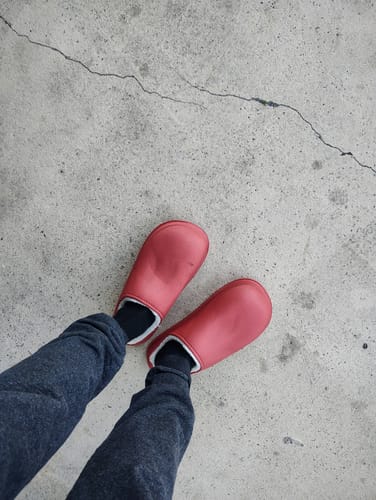 Reviewer wearing red, fur-lined Cloud Slides clogs while standing on concrete.