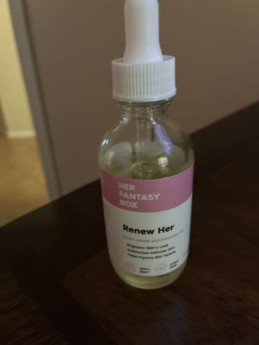 A customer's bottle of Her Fantasy Box Renew Her Yoni Oil with a white dropper, on a wooden surface.