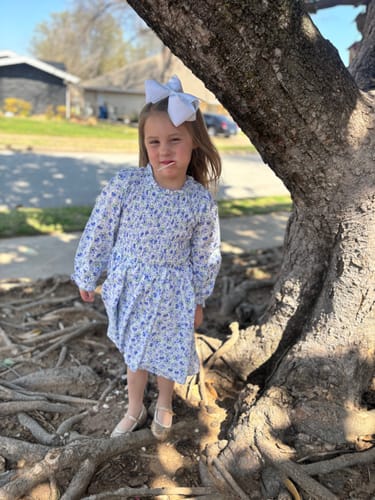 Customer wearing the floral, long-sleeved Duke Garden Blue Ariella Dress with a smocked bodice while standing outdoors.