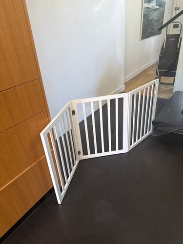 Reviewer's white Wooden Pet Gate set up in a flexible zig-zag shape to block a hallway.