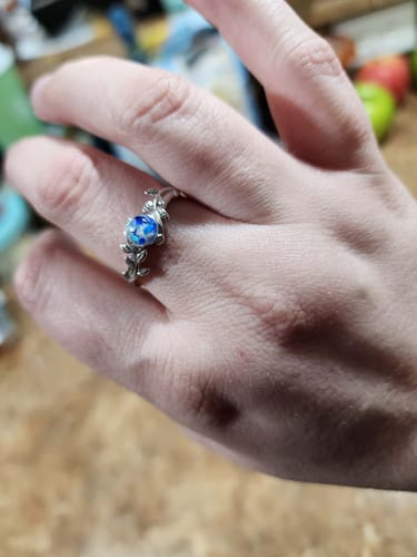 Reviewer's hand wearing a Leaf Opal Cremation Ring with a silver leaf band and a round blue and white infused bezel.