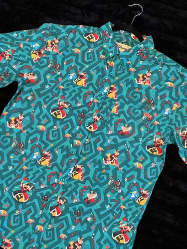 Reviewer's teal Disney "Off with Their Heads!" shirt on a hanger, showing the all-over Alice in Wonderland pattern.