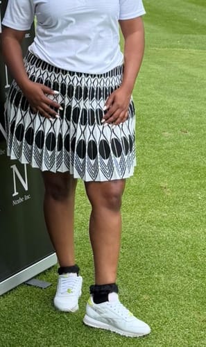 Reviewer wearing the white sleeveless shirt and patterned pleated skirt suit while standing on grass.