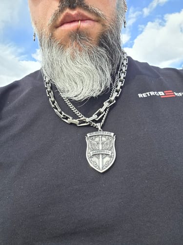 Customer wearing the solid St. Michael's Shield Necklace, layered with other chains against a black shirt.