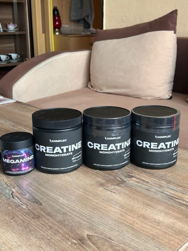 A reviewer's tub of MegaMind and three tubs of creatine from the same brand lined up on a wooden table.