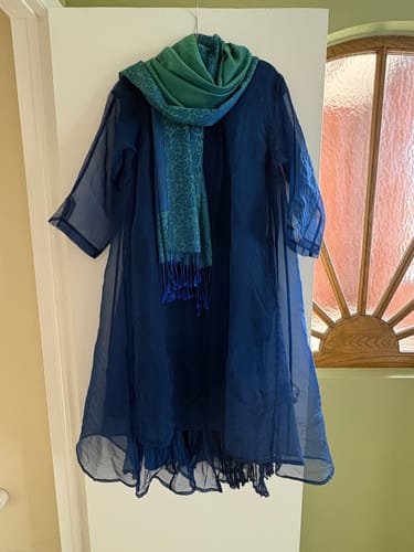 Customer's flowy cobalt blue dress hanging on a door with a scarf.