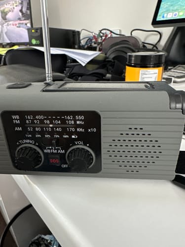 Customer's grey portable emergency radio with an extended antenna, showing its tuning and volume knobs on a desk.
