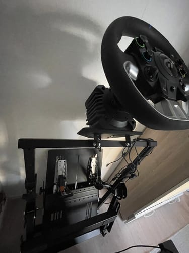 A reviewer's black APEX Wheel Stand shown fully assembled with a steering wheel and pedals in a room.