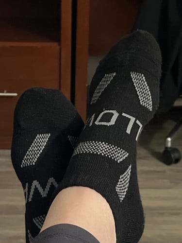 Customer's feet propped up, showing the patterned soles of their black Men's Alpaca ankle socks.