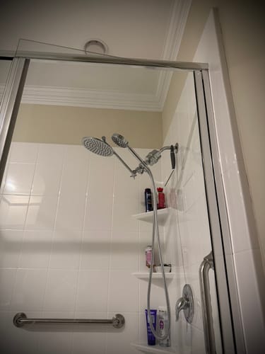 Customer's installed dual shower head with an adjustable arm and filter in a white tiled shower.