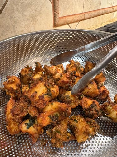 Customer's cooked and seasoned Halal Beef Cubes resting in a metal colander with tongs.