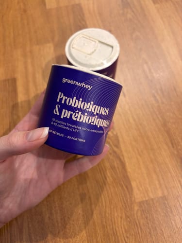 Client tenant le pot bleu de Probiotiques & Prébiotiques dans sa main sur un fond en bois.