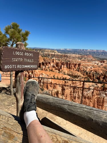 Reviewer's black Smart I Barefoot Shoe propped on a railing overlooking a canyon, near a sign recommending boots.