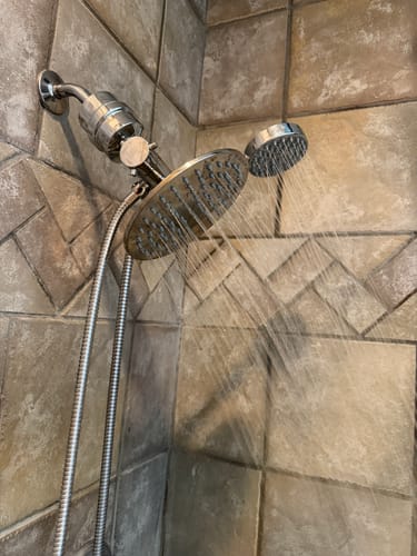 Customer's inline shower filter installed on a dual head shower fixture, shown with water running in a tiled shower.