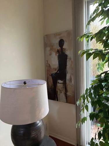 Customer's large Waiting Figure Abstract Wall Art hanging in a room's corner next to a lamp and plant.