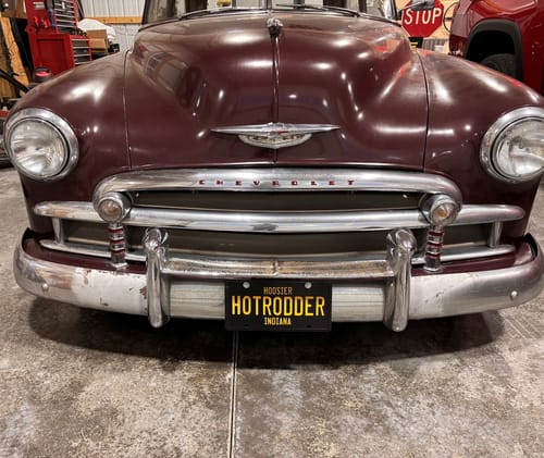 Reviewer's custom black and yellow license plate with 'HOTRODDER' text mounted on the bumper of a classic maroon car.