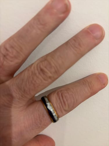 A customer's hand wearing the Guardian ring with its shiny rose gold band and detailed inlays.