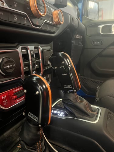 Customer's two black Hill Killer Transmission Shifters with orange accents installed in a Jeep's center console.