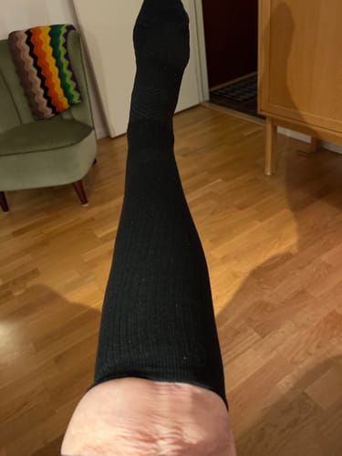 En kund som bär en lång, svart Diasocks stödstrumpa på sitt ben inomhus.