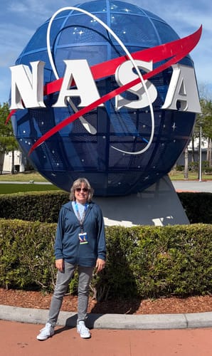 Reviewer wearing the zip-up Ryann Hoodie in Starry Night while standing in front of a large NASA logo.