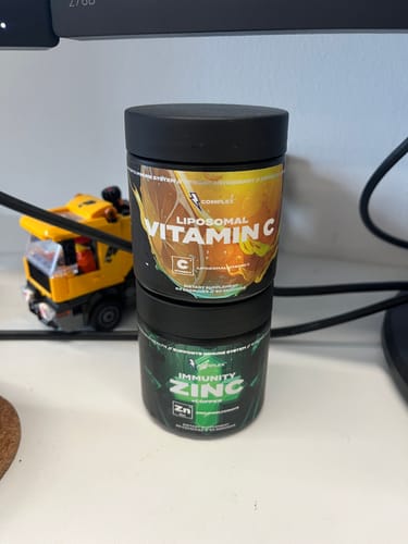 Customer's jar of Immunity Zinc stacked underneath a Liposomal Vitamin C supplement on a desk.
