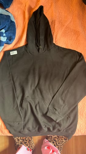 Customer's plain black College hoodie laid out on a bed before customization.