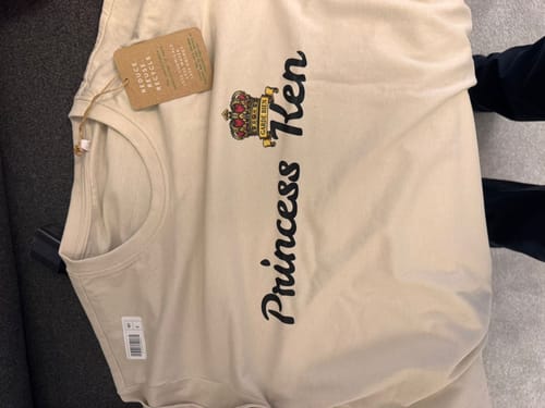 Customer's cream-colored t-shirt with a 'Princess Ken' graphic and crown, laid out with its tag still attached.