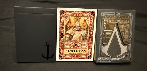 Customer displays three collectible card decks from their Mystery Deck: False Anchors, Fortress, and Assassin's Creed.