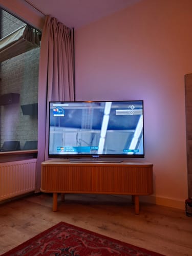 Recensent toont het naturel Mailen tv-meubel in een woonkamer met een televisie erop.