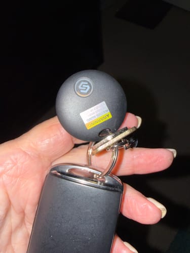 Reviewer holding the small, black SmartTag attached to a car key fob on a keyring.
