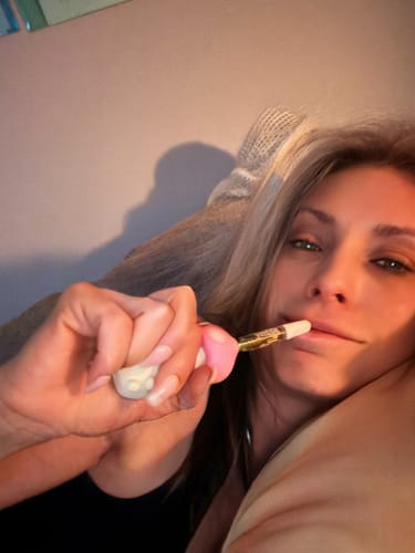 Reviewer holding a small white and pink vape pen to their mouth.