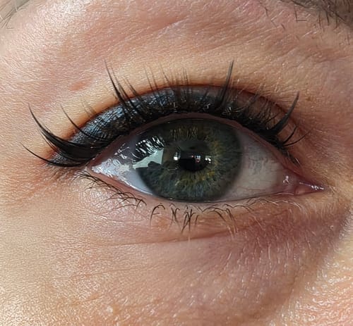Nahaufnahme des Auges einer Kundin, die zeigt, wie ihre Wimpernverlängerungen mit dem Top Coat Sealer halten.