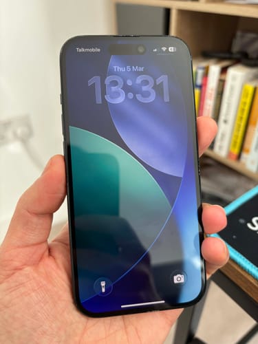 Customer holding their black refurbished Apple iPhone 15, which is on and shows the lock screen in excellent condition.