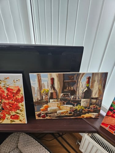 Customer's completed Wine and Cheese Delight painting displayed on a shelf, showing the detailed still life scene.