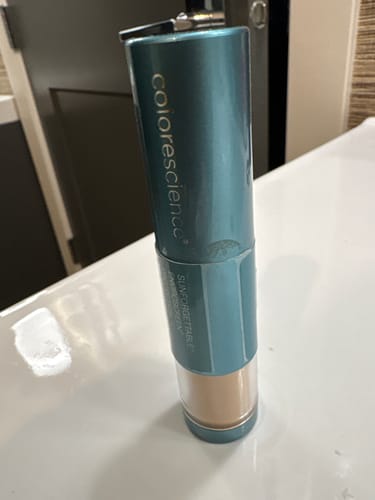 A customer's Colorescience Sunforgettable Brush-On Shield SPF 50 in its teal tube, resting on a white countertop.