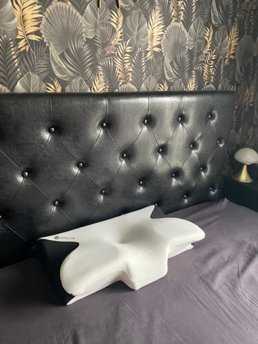 Le client montre le coussin d'alignement cervical Cellsius, blanc et noir, posé sur un lit.