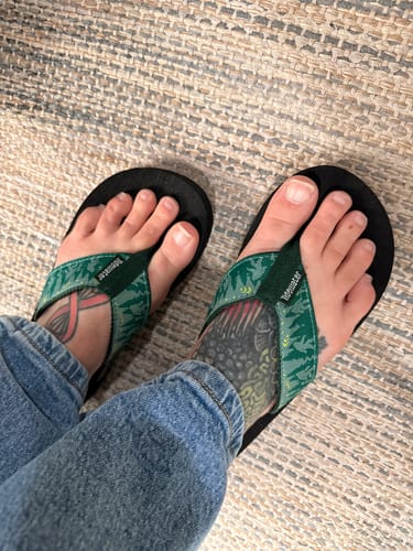 Customer's feet wearing the Bigfoot and Co flip flops with patterned green straps and black soles.