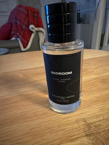 Customer's bottle of Redroom Eau de Parfum by Thomson Carter on a wooden table.
