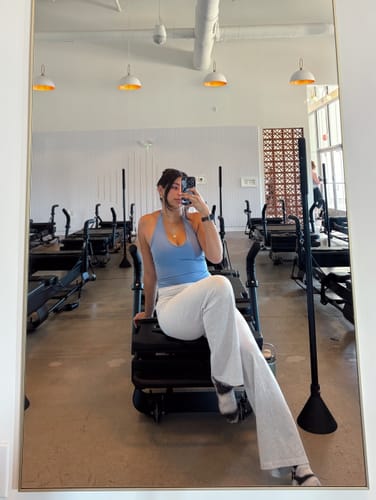 Reviewer in a pilates studio taking a mirror selfie, showing the flattering fit of the French-Blue Halter Tank.