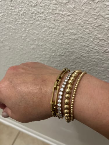 Reviewer's hand displaying the gold Lovers Chain Bracelet stacked with a tennis bracelet and two beaded bracelets.