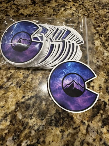 Customer's custom stickers with a purple galaxy design in the shape of a Colorado 'C' logo, displayed on a countertop.