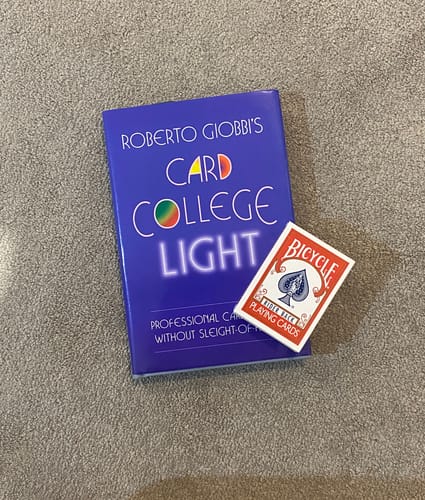 Customer's 'Card College Light' book lying on a carpet next to a red deck of playing cards.