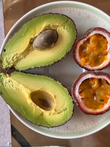 Kunde zeigt eine aufgeschnittene Baby-Avocado und zwei Passionsfrüchte auf einem weißen Teller.